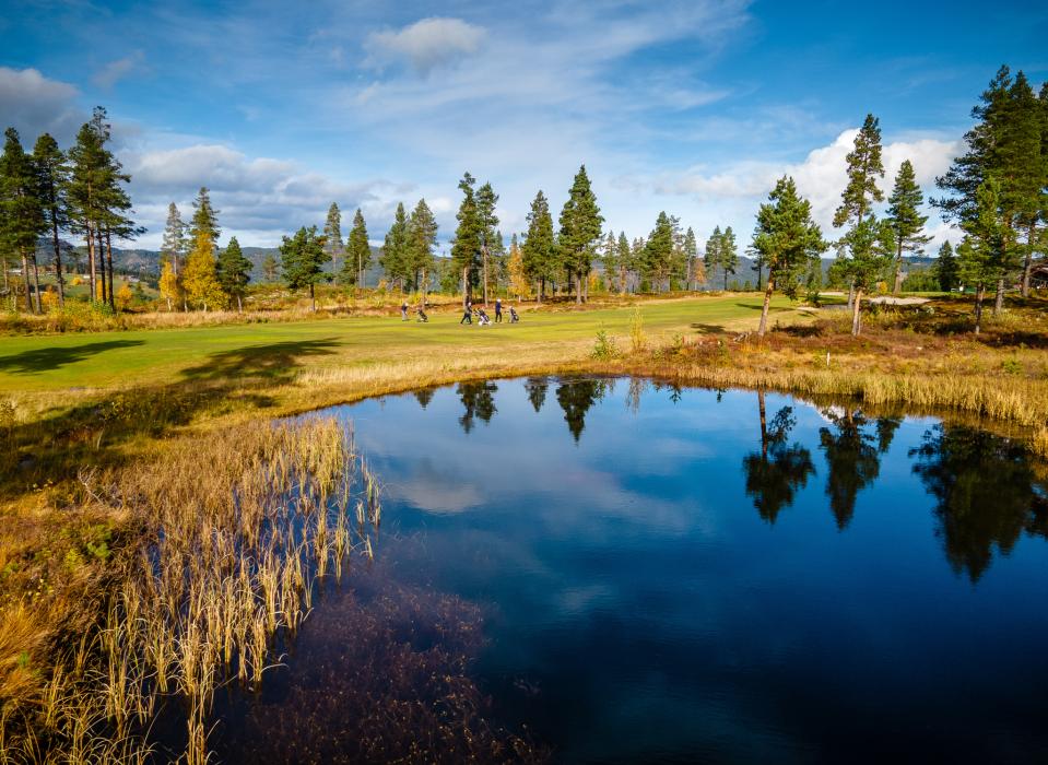 En vakker sø som speiler landskapet midt på golfbanen. Et rolig og naturnært innslag i spillet.