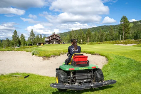 en person som kjører gressklipper på en golfbane