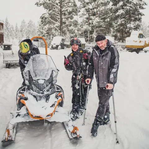 En gruppe mennesker som står ved siden av en snøscooter